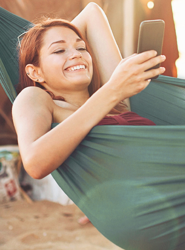 Banking anywhere. Girl in hammock using phone.