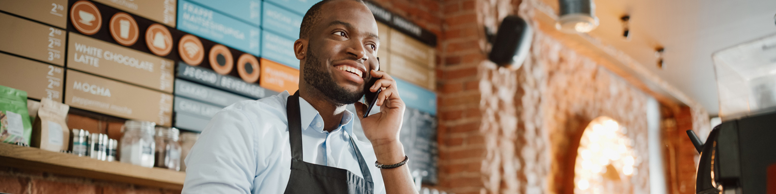 A male employee on the phone at a coffee shop. 