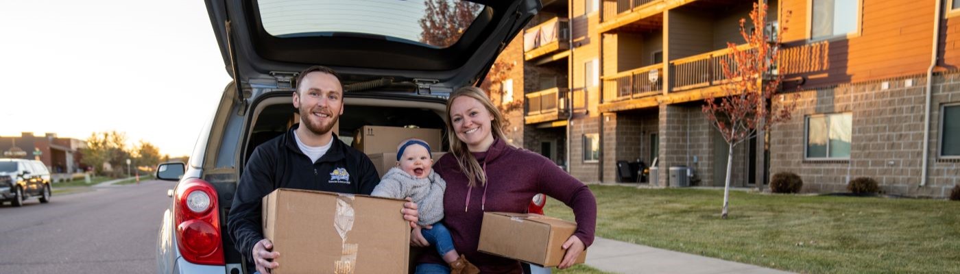 Family with moving boxes near back of vehicle. 